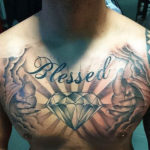 tatoeage van een grote diamand met daarboven "blessed" en er omheen lichtstralen en twee handen die uit wolken lijken te komen