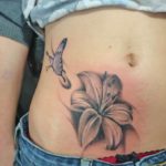 Vrolijke tattoo op de onderbuik met een lelie en een paarse vlinder