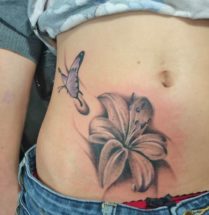 Vrolijke tattoo op de onderbuik met een lelie en een paarse vlinder