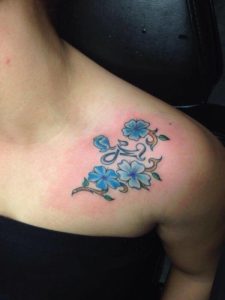 Kleine blauwe bloemen met het moeder en dochter symbool erin verwerkt geplaatst op de schouder