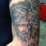 tatoeage van Jezus met dornen kroon en rozen geplaatst op de bovenarm