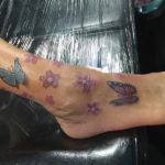 tatoeage van kleine paarse bloemetjes en twee vlinder op de voet