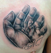 tattoo van een klein baby handje in een grotere hand met de initialen MJ eronder