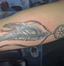tattoo van twee veren die aan een kleine dromenvanger hangen in de black and grey stijl