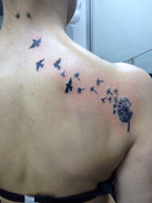 Tattoo van een uitgebloeide paardenbloem waar zwaluw vogels vanaf vliegen, geplaatst op de schouder en nek.